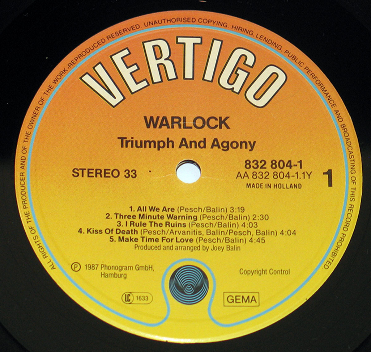 Close-up of the 'Triumph and Agony' vinyl record label by Warlock, featuring the iconic Vertigo logo on an orange-to-yellow gradient background, with tracklist and production details in bold black text, made in Holland.